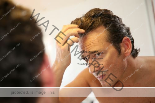 A man in front of a bathroom mirror, worried about his thinning hairline