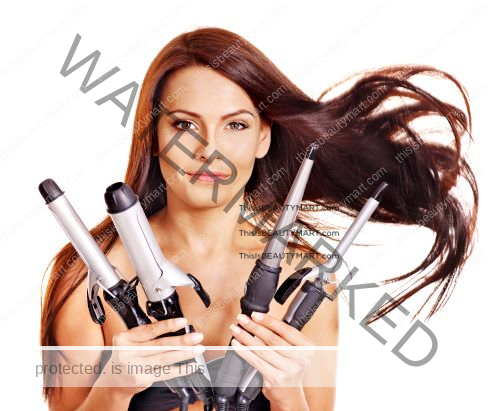 A woman holding four different curling irons while her hair is blowing in the air