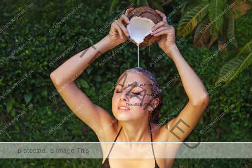 A woman pouring coconut milk on her head directly from coconut shells