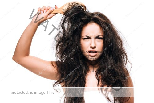 A woman with a distressed face as her hair brush is caught in her long and unruly hair