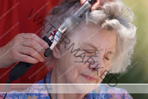 An elderly caucasian woman getting her hair curled by a hair stylist using a curling iron