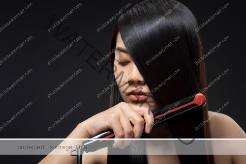 Asian woman straightening her hair with a red and black flat iron