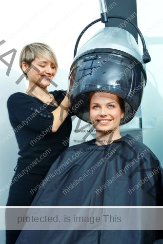 At the salon, a female customer using the hooded hair dryer assisted by the beautician