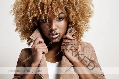 Black woman with curly hair dyed blonde, posing fashionably with a brown jacket