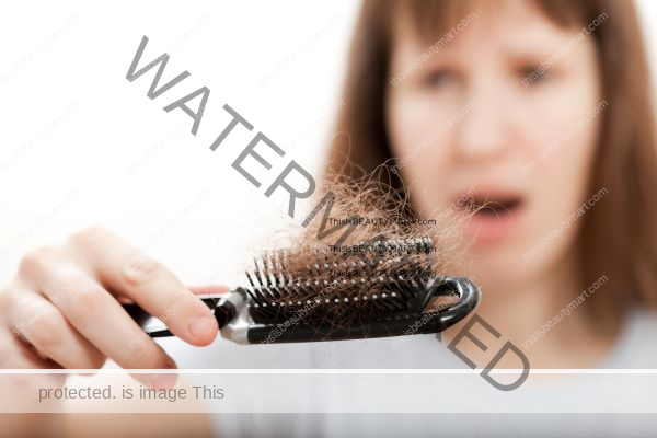 Close up of a hair brush with shedding hair caught and the woman holding the brush blurred in the background while in shock