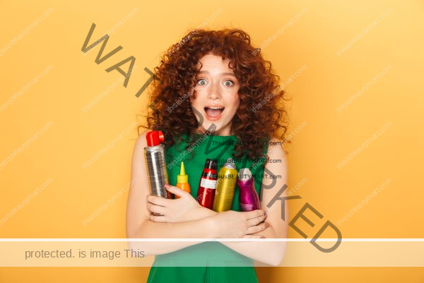 Red and curly haired woman holding several bottles of curly hair products