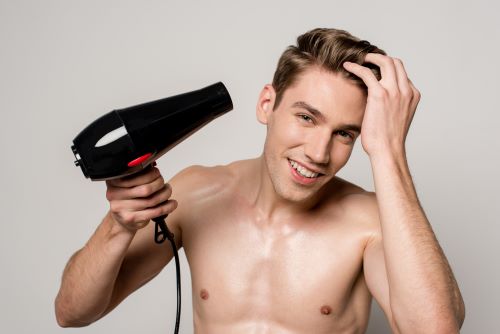 Shirtless man happily using a hair dryer on his head