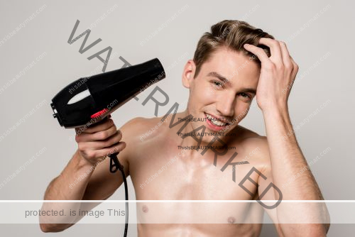 Shirtless man happily using a hair dryer on his head