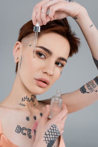 Short-haired tattooed woman applying beauty serum to moisturize her face