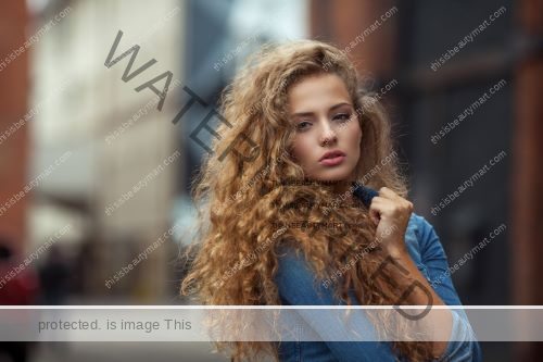 Woman with orange perm hair wearing denim jacket and posing outdoors in daylight