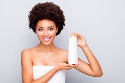 Woman with short curly hair holding a bottle of hair conditioner while she is in her bath towel