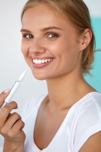 Woman smiling while holding a teeth whitening pen